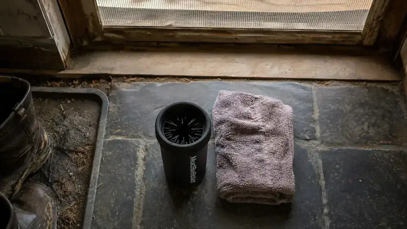A MudBuster paw cleaner and a folded towel set side by side on a slate mudroom floor