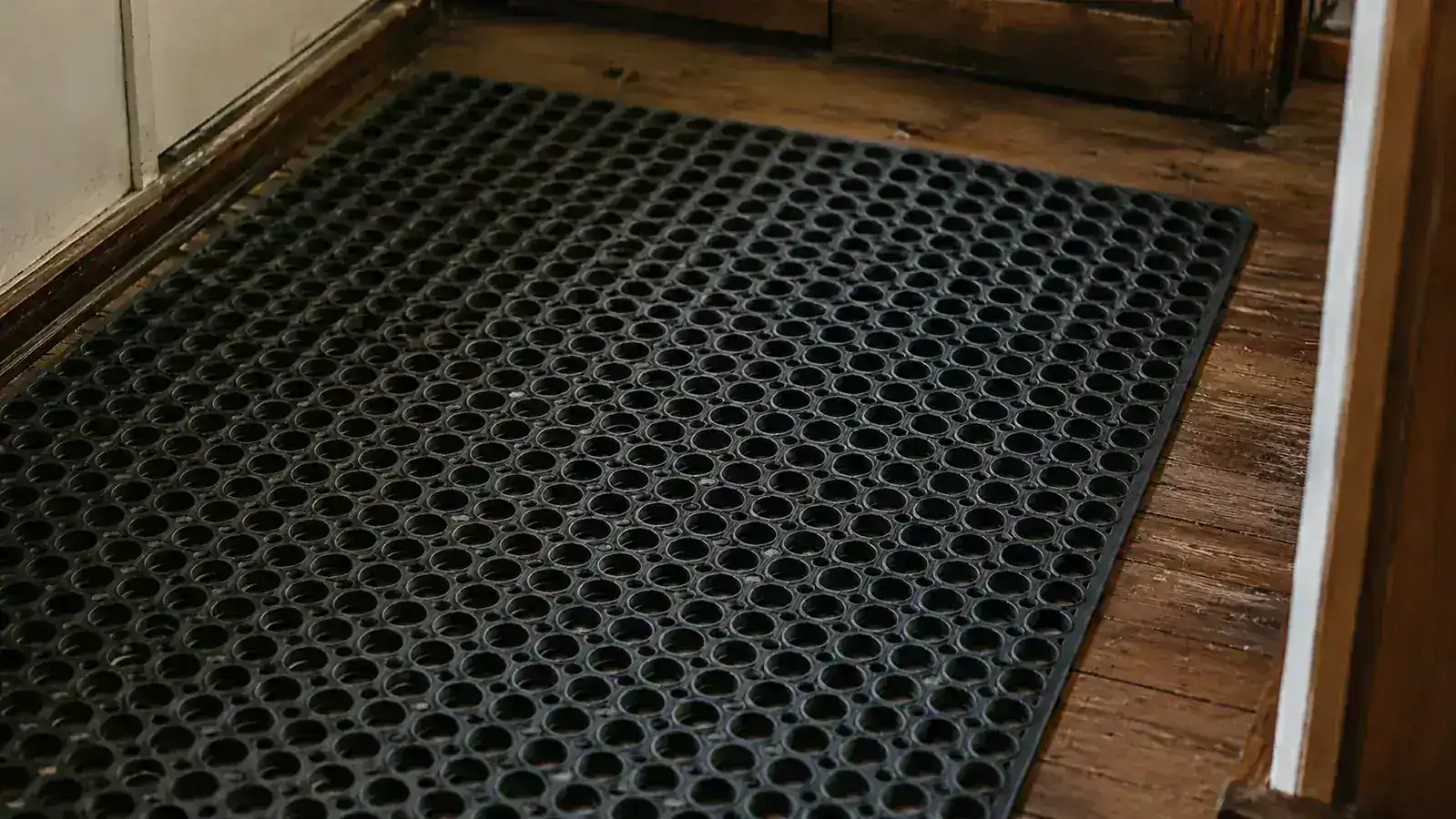 Close-up of a gray honeycomb litter mat with visible hexagonal holes on a wood hallway floor
